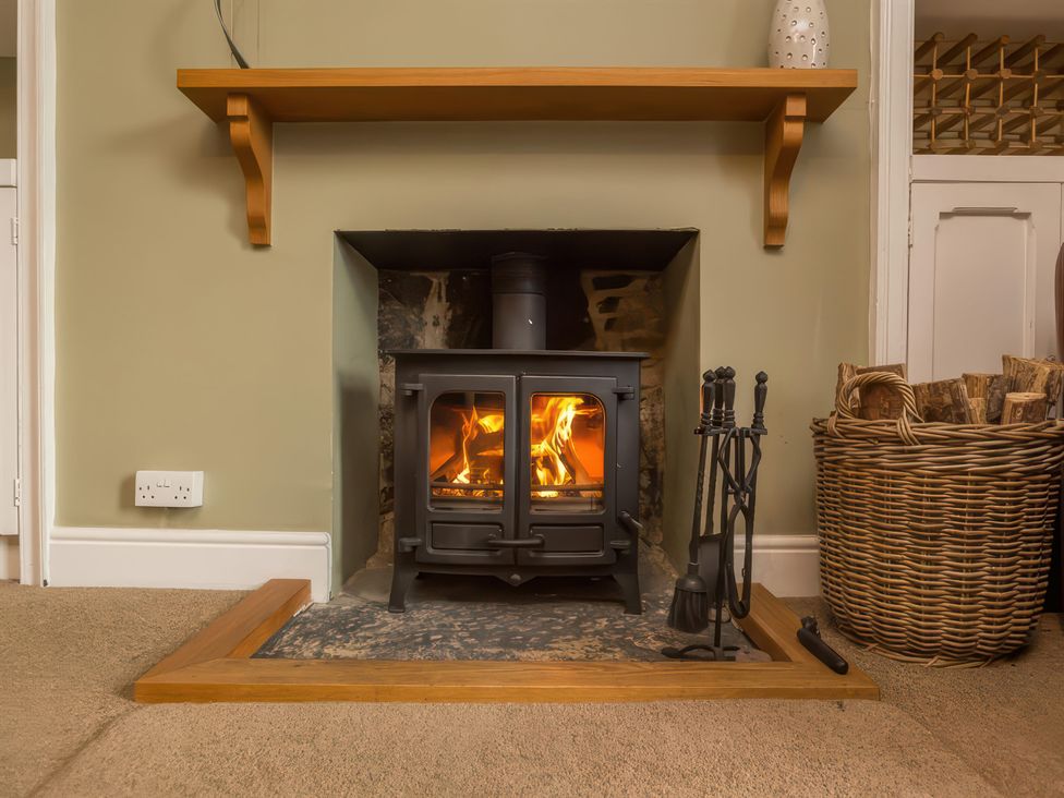 A fireplace with a wood stove and firewood basket at River Cottage in Inverness
