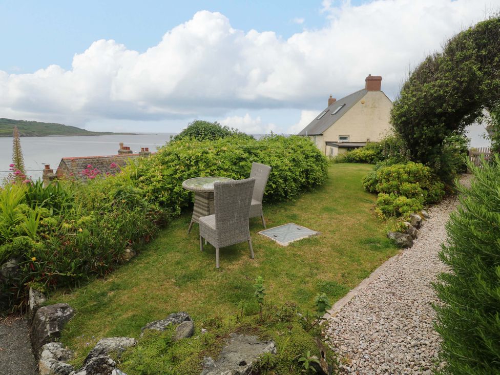 A garden with a table and chairs overlooking water at Mermaid Cottage in Coverack near St Keverne