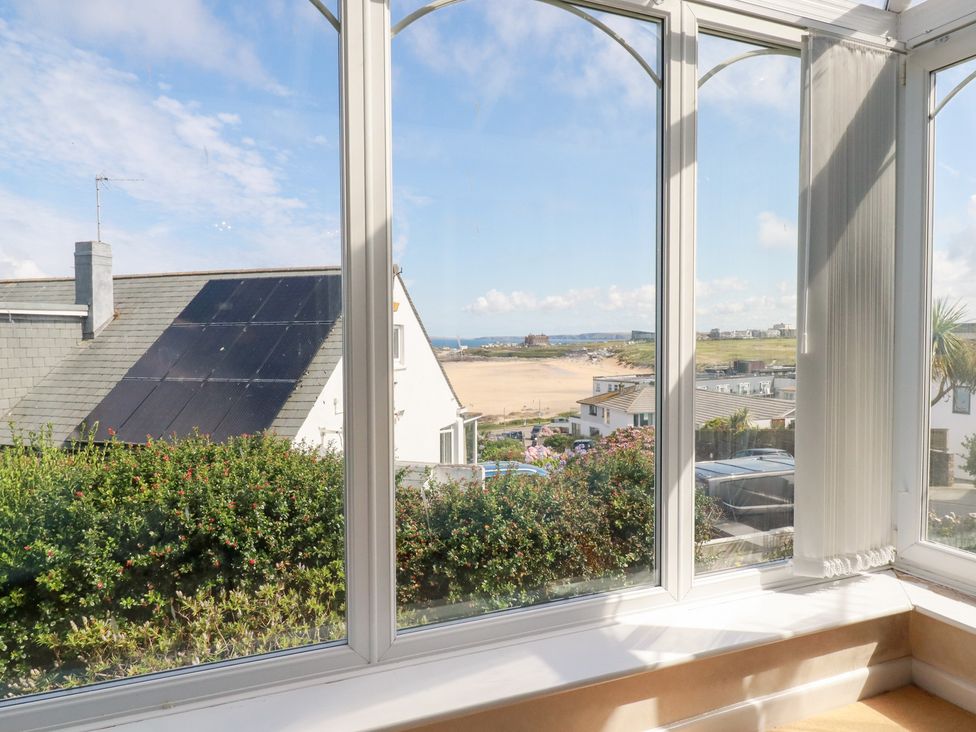 A conservatory with a view of a beach and houses at 22 Pentire Avenue in Newquay