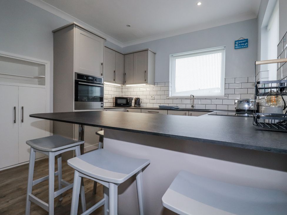 A kitchen with cabinets, appliances and bar stools at Pipers in Newquay