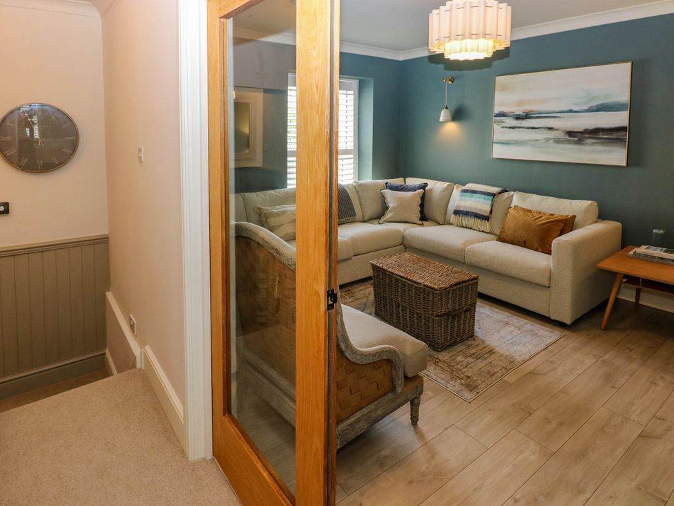 A living room with a beige sectional sofa pillows wicker coffee table wooden side table and a wall clock at The Loft in Ystradgynlais
