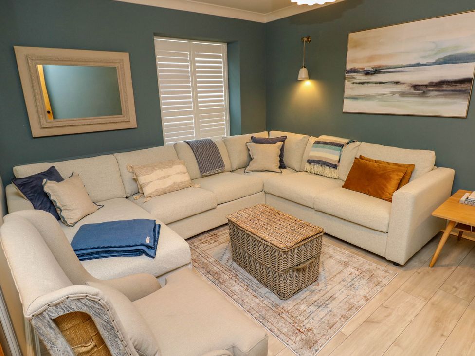 A living room with an L-shaped sofa a wicker coffee table an armchair and a wall painting at The Loft in Ystradgynlais