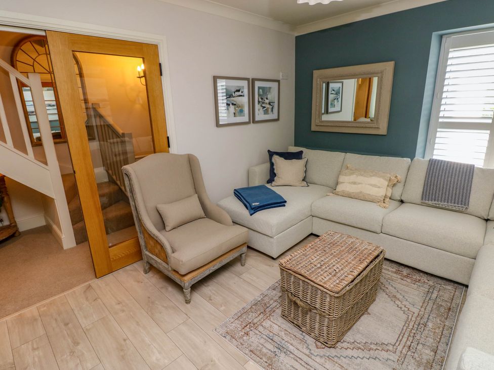 A living room with a beige armchair a sectional sofa and a wicker storage chest on a rug at The Loft in Ystradgynlais