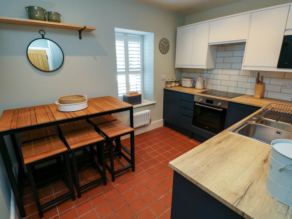 A kitchen with wooden stools and table a round mirror white cabinets and cooking appliances at The Loft in Ystradgynlais