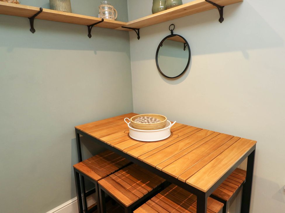 A wooden table with matching stools underneath a wall shelf with decorative items and a round mirror on the wall at The Loft in Ystradgynlais