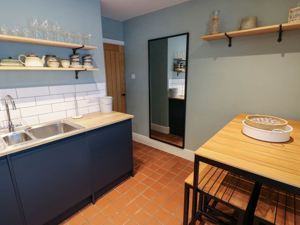A kitchen with a double sink and shelves with cups and glasses and a wooden table with stools at The Loft in Ystradgynlais