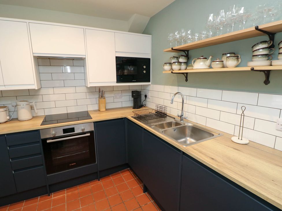 A kitchen with dark lower cabinets and white upper cabinets with a built-in oven and microwave a double sink wooden countertops white tiled backsplash and shelves holding teapots cups plates and glasses at The Loft in Ystradgynlais
