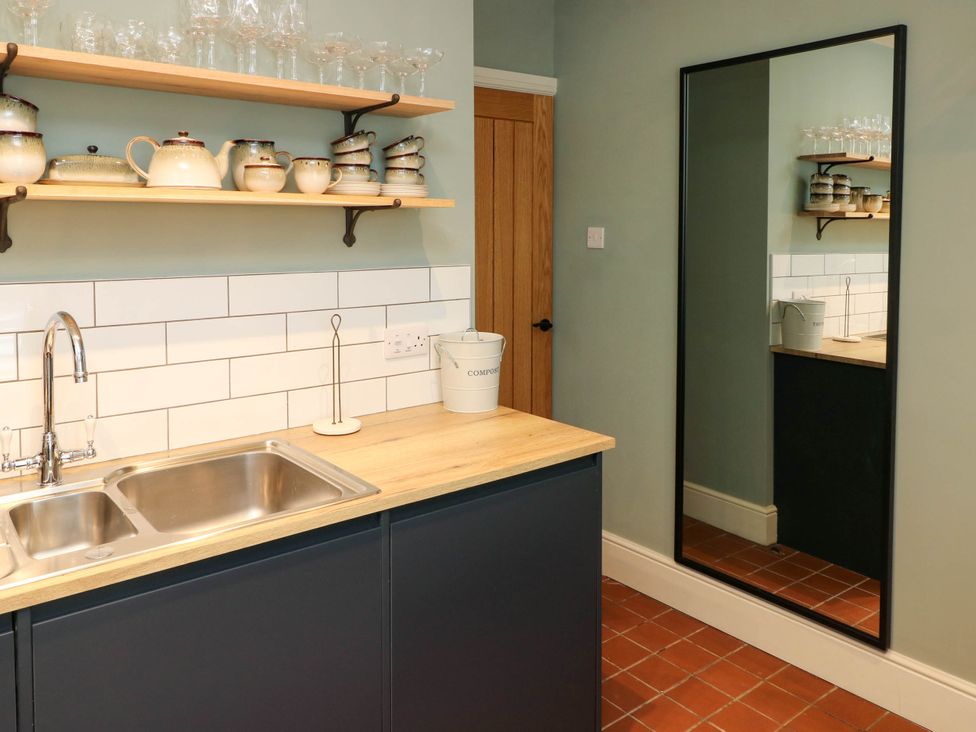 A kitchen area with a double sink wooden countertop shelves with cups and glasses a compost bin and a large wall mirror at The Loft in Ystradgynlais