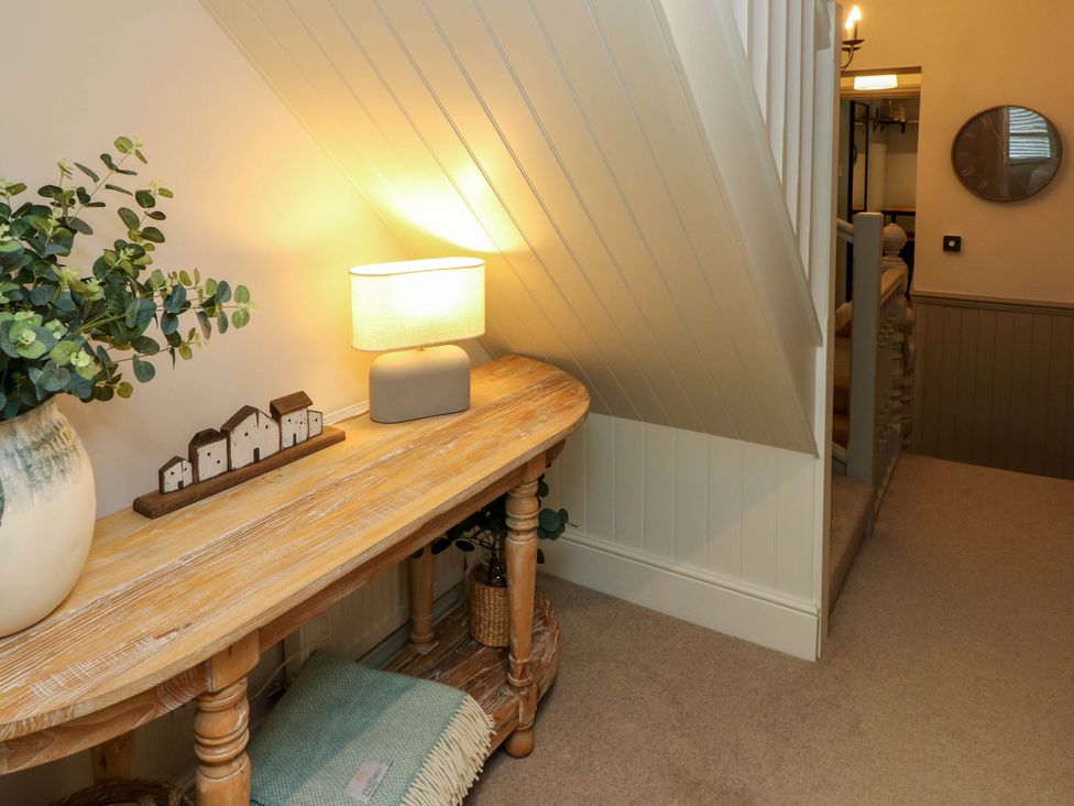 A hallway with a wooden table holding a lamp, decorative houses, and a vase of greenery at The Loft in Ystradgynlais