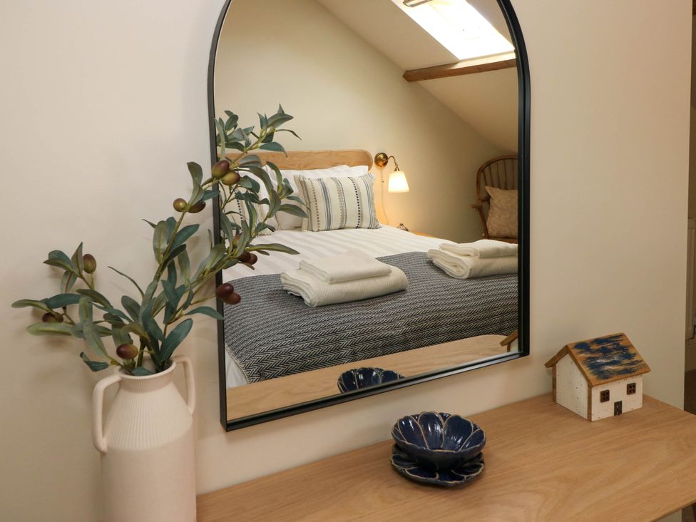 A wooden desk with a vase of olive branches a small decorative house and blue ceramic bowls in front of a mirror reflecting a bed with towels and a wall lamp at The Loft in Ystradgynlais