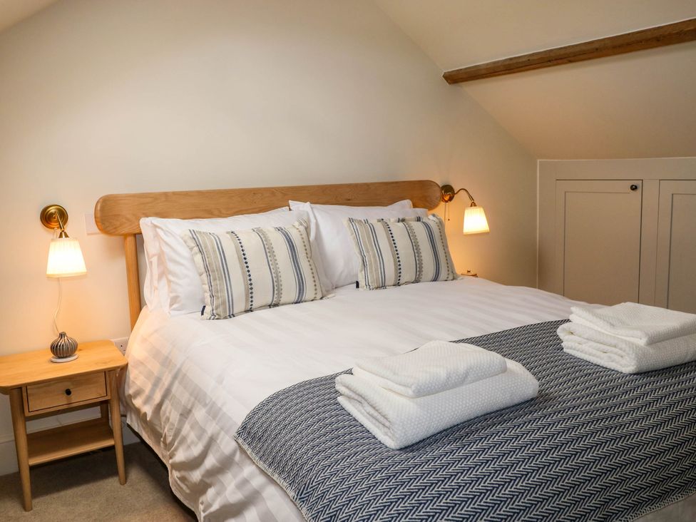 A bedroom with a wooden bed frame white bedding striped pillows bedside tables with lamps and folded towels on the bed at The Loft in Ystradgynlais