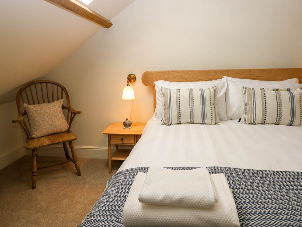 A bedroom with a wooden chair, a bedside table with a lamp, and a bed with striped pillows and folded towels at The Loft in Ystradgynlais