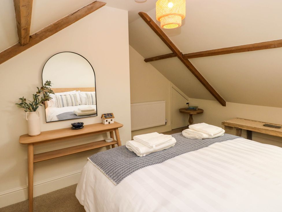 A bedroom with a bed two folded towels on a blanket a wooden console table with a mirror and a vase a small round side table and a wooden bench at The Loft in Ystradgynlais