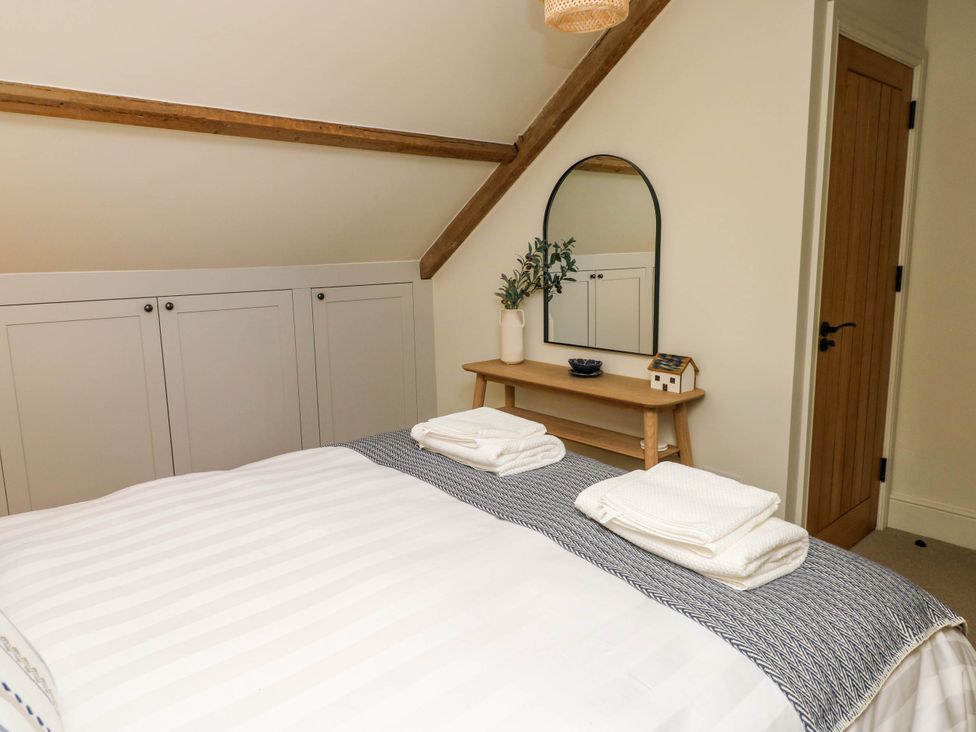 A bedroom with a bed, a wooden bench with a mirror above it, a vase with greenery, and a wooden door at The Loft in Ystradgynlais