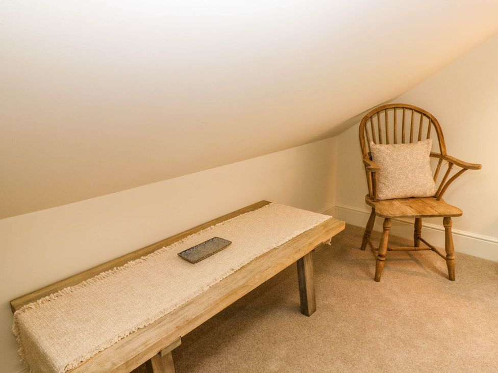 A wooden chair with a cushion and a wooden table with a runner and a tray in a room with sloped ceiling at The Loft in Ystradgynlais