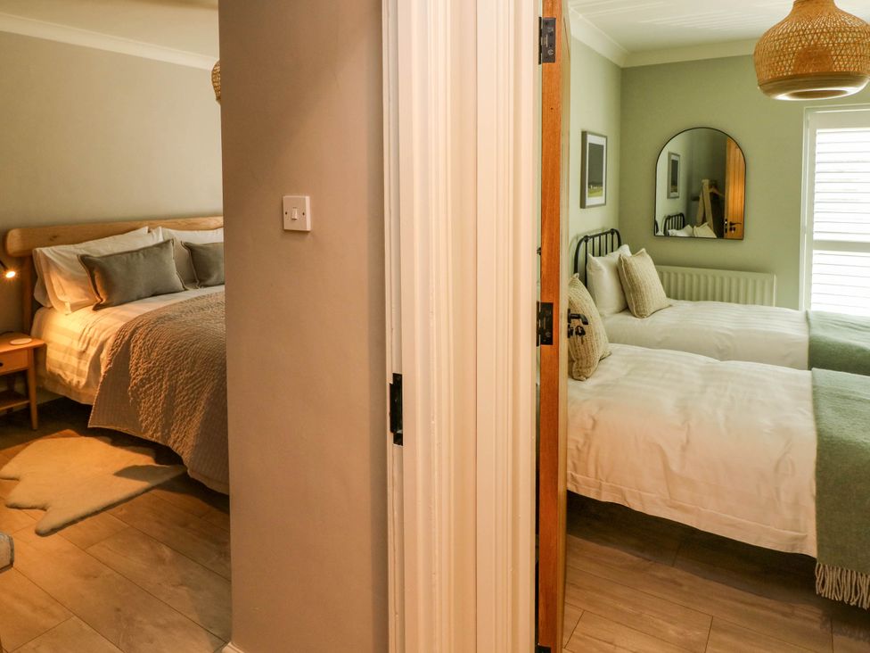 Two adjacent bedrooms separated by a wall one with a double bed and side table the other with two single beds and a wall mirror at The Loft in Ystradgynlais