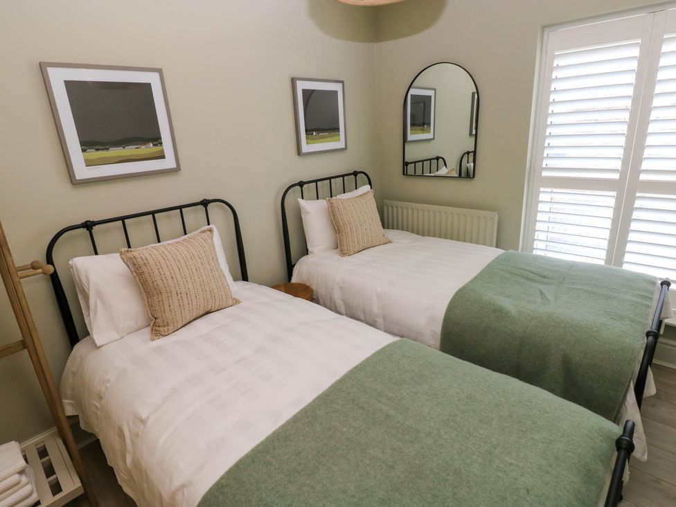 A bedroom with two single beds with green blankets and pillows a mirror and framed pictures on the wall at The Loft in Ystradgynlais