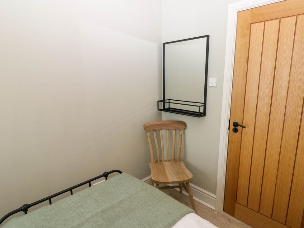 A small bedroom corner with a wooden chair a black framed wall mirror and a wooden door at The Loft in Ystradgynlais