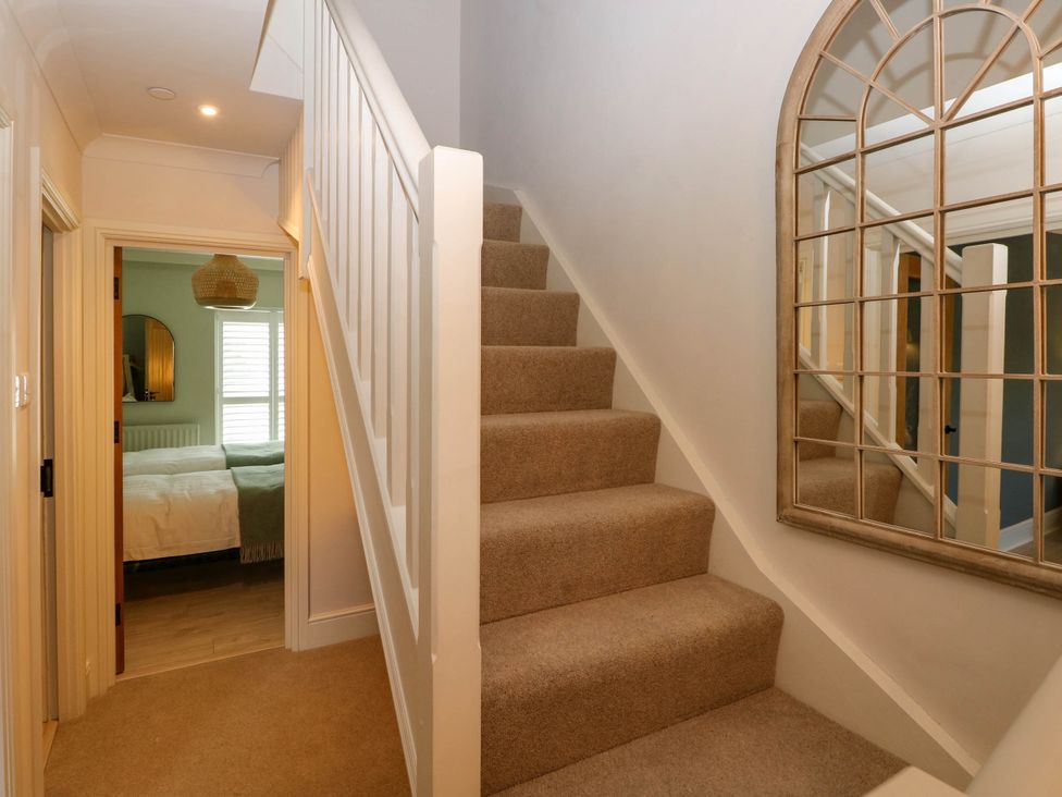 A carpeted staircase with white railing and a large wall mirror in a hallway showing a bedroom through a door at The Loft in Ystradgynlais