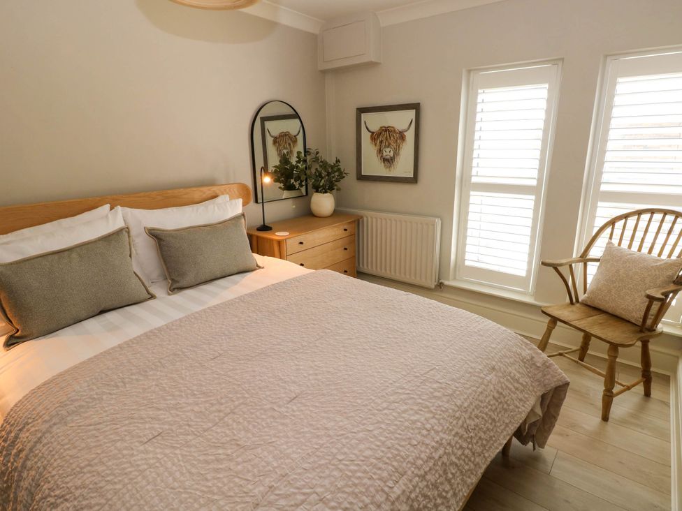 A bedroom with a bed a wooden chair with a pillow a dresser with a mirror and a potted plant and a framed picture on the wall at The Loft in Ystradgynlais