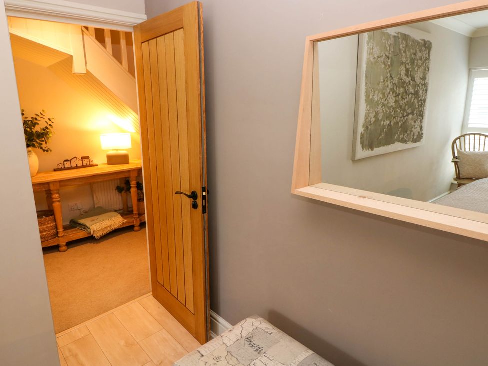 A wooden door open to a lit room with a table lamp on a wooden table and a large mirror on the wall reflecting a chair and wall art at The Loft in Ystradgynlais