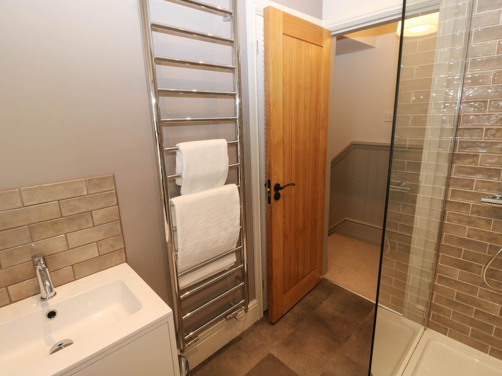 A bathroom with a sink, towel radiator with towels, wooden door, and a glass shower enclosure at The Loft in Ystradgynlais