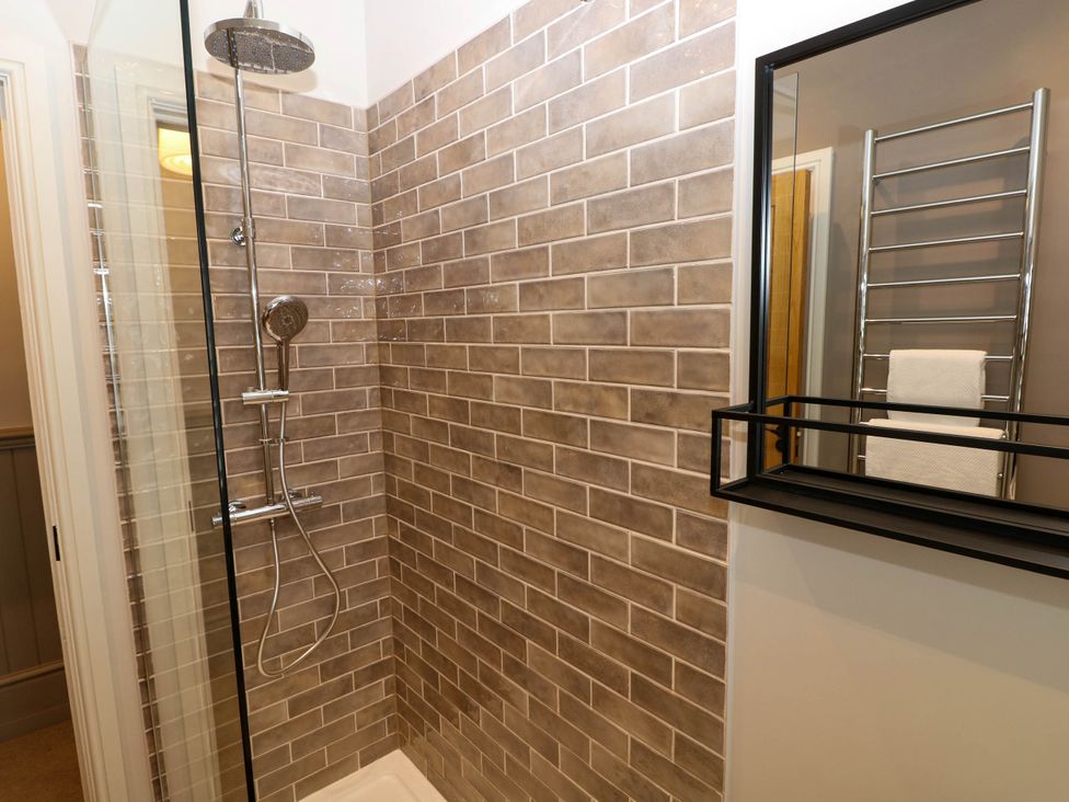 A bathroom shower area with brown tiled walls a chrome shower head and handheld shower and a mirror with a towel rack reflected at The Loft in Ystradgynlais