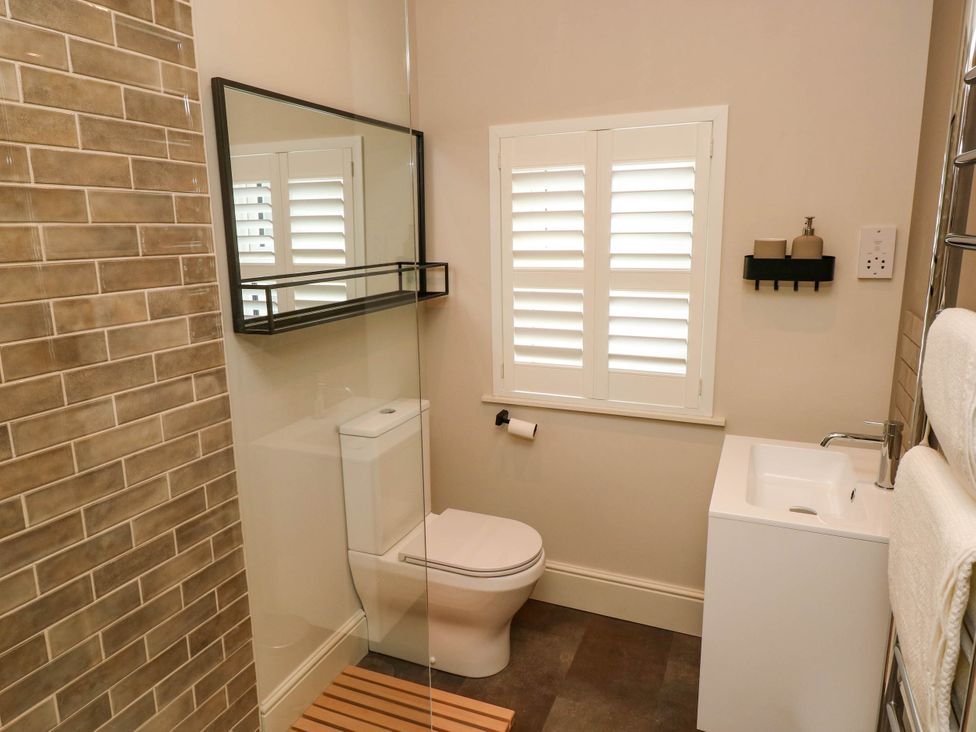 A bathroom with a toilet, sink, mirror, and window with shutters at The Loft in Ystradgynlais