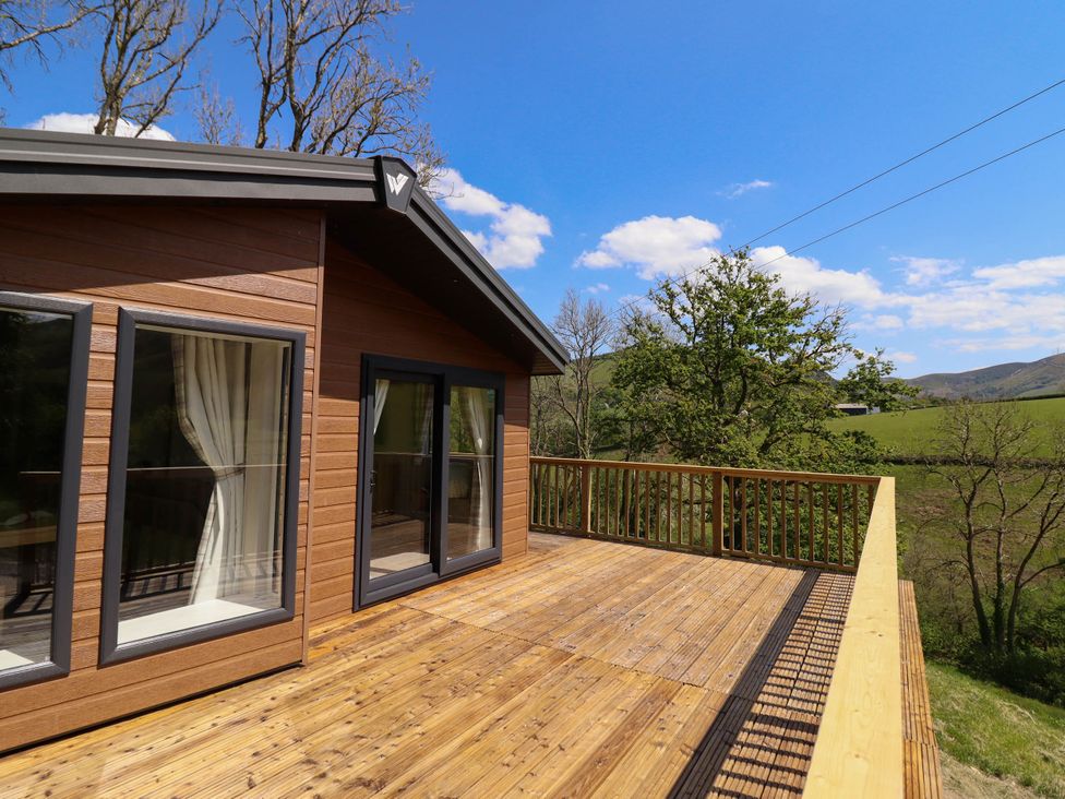 A wooden deck attached to a house with glass doors and windows overlooking fields and trees at The Owlet in Dolwen near Llanidloes