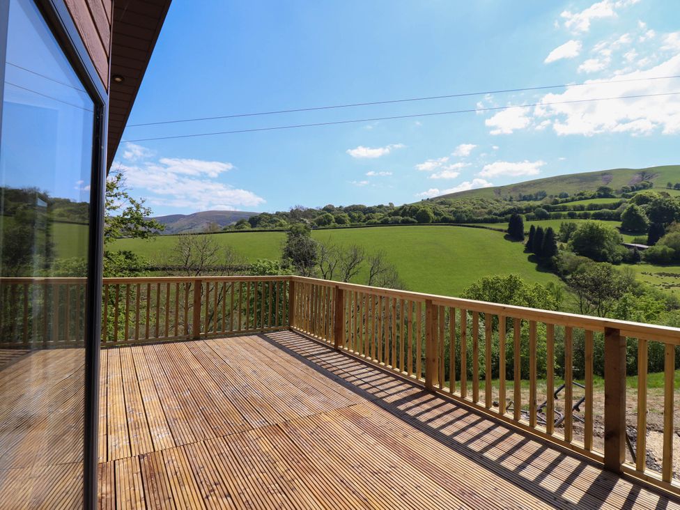 A wooden balcony overlooking green hills and trees at The Owlet in Dolwen near Llanidloes
