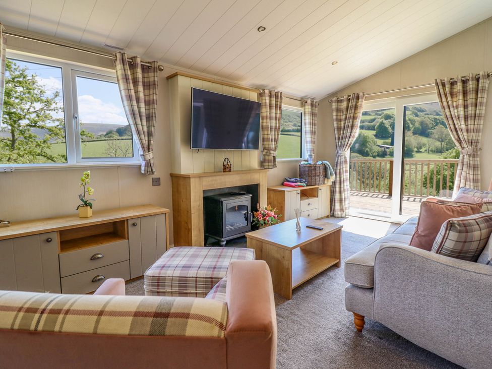 A living room with a sofa armchairs a coffee table and a TV mounted above a fireplace at The Owlet in Dolwen near Llanidloes