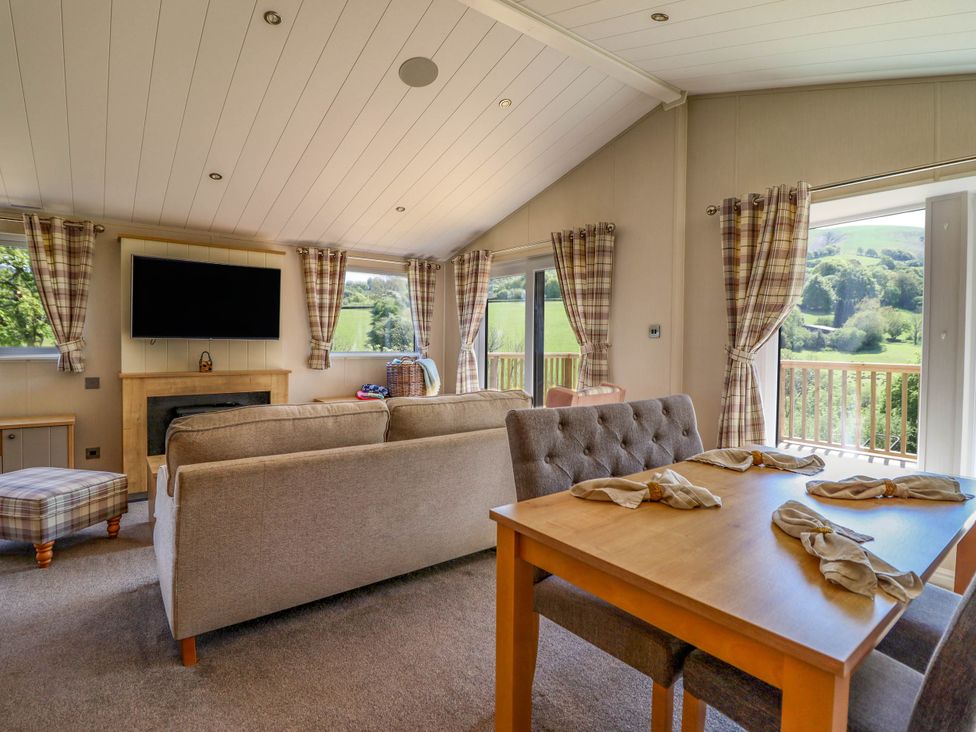 A living room with a sofa a television and windows with plaid curtains at The Owlet in Dolwen near Llanidloes