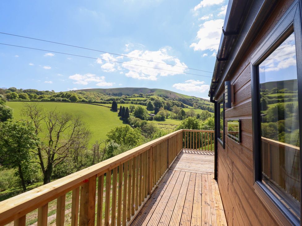 A wooden balcony attached to a cabin overlooking green rolling hills and trees at The Owlet in Dolwen near Llanidloes