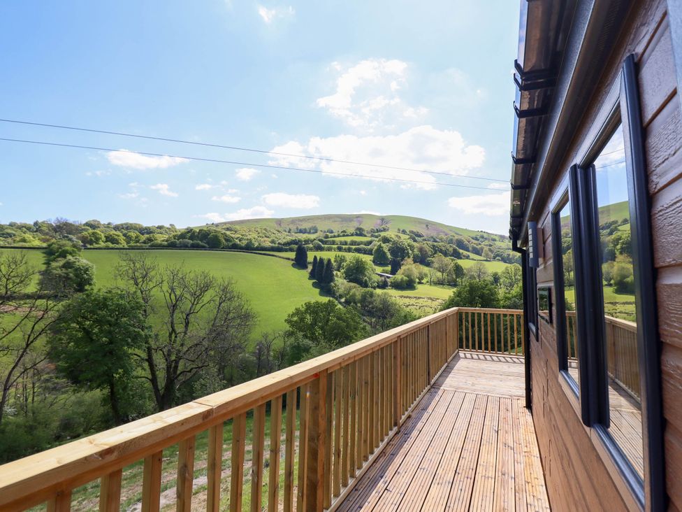 A wooden deck with railing attached to a building overlooking green hills and trees at The Owlet in Dolwen near Llanidloes