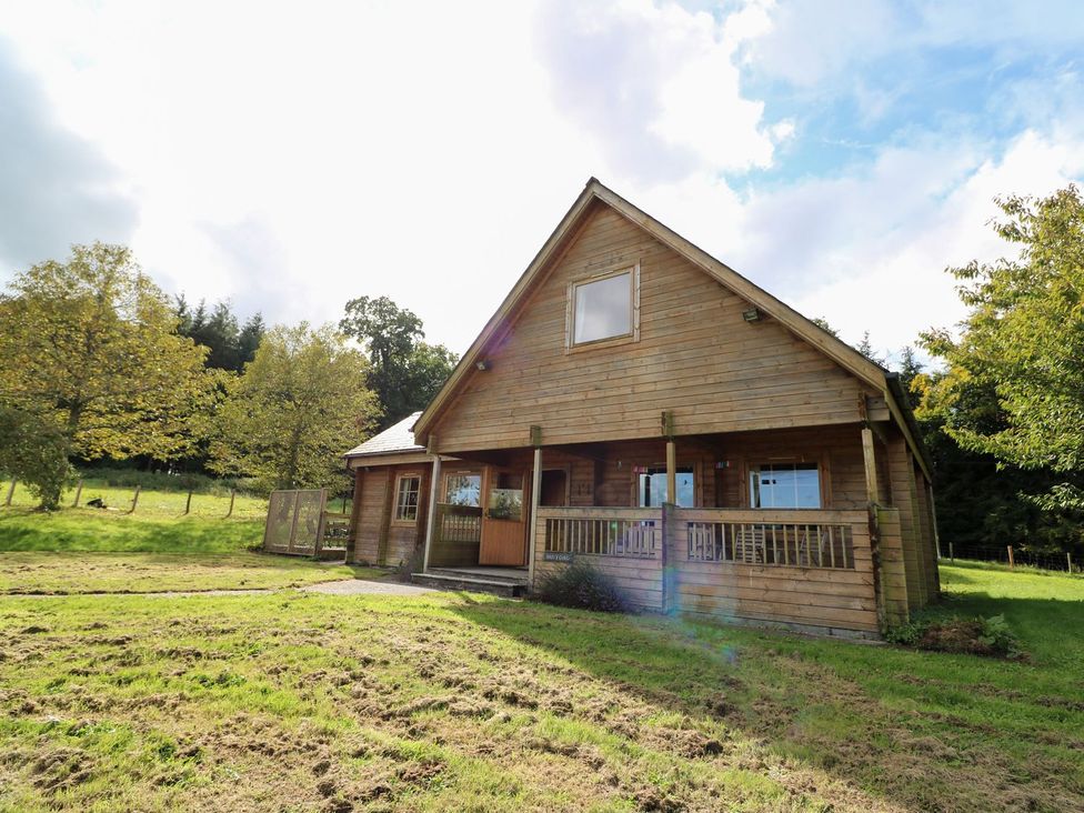 A wooden house with a veranda and surrounding trees at Dan Y Coed near Beggar's Bush near Presteigne