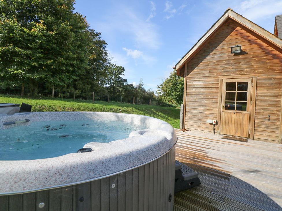 An outdoor area with a hot tub near a wooden cabin at Dan Y Coed in Beggar's Bush near Presteigne