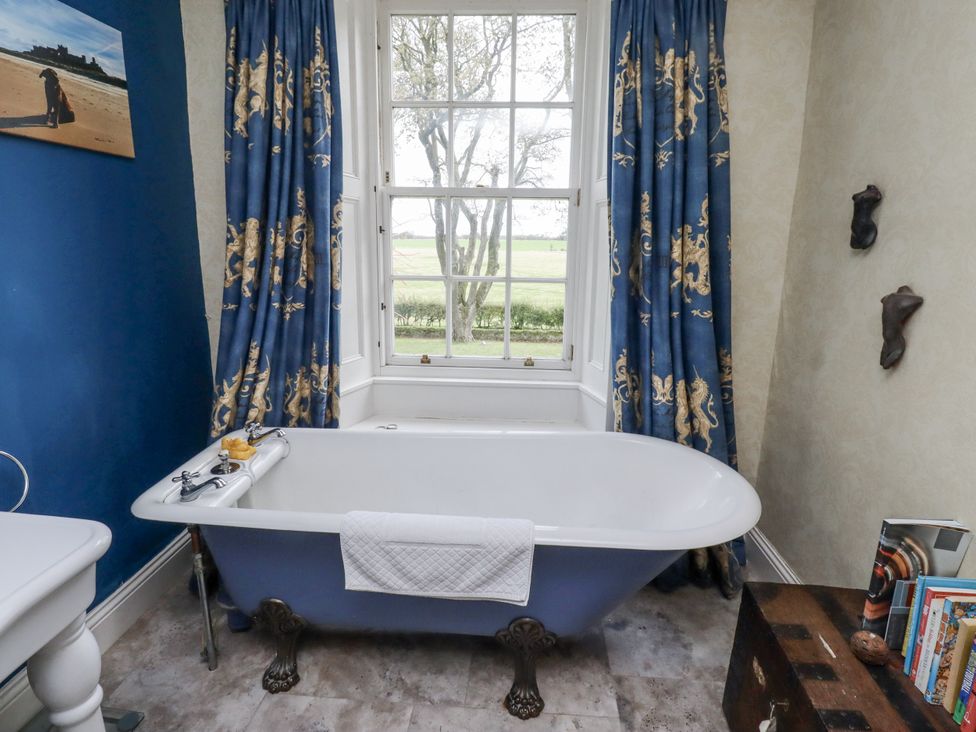 A bathroom with a bathtub and curtains at Elford Farmhouse in Seahouses