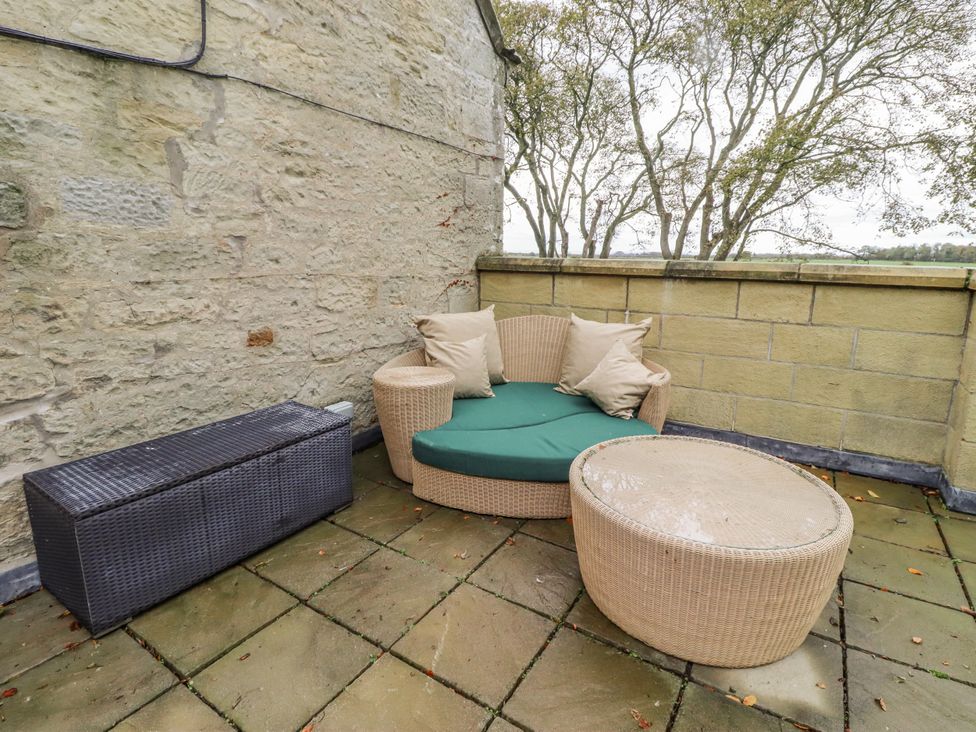 An outdoor patio with a sofa, round table, and storage box at Elford Farmhouse in Seahouses