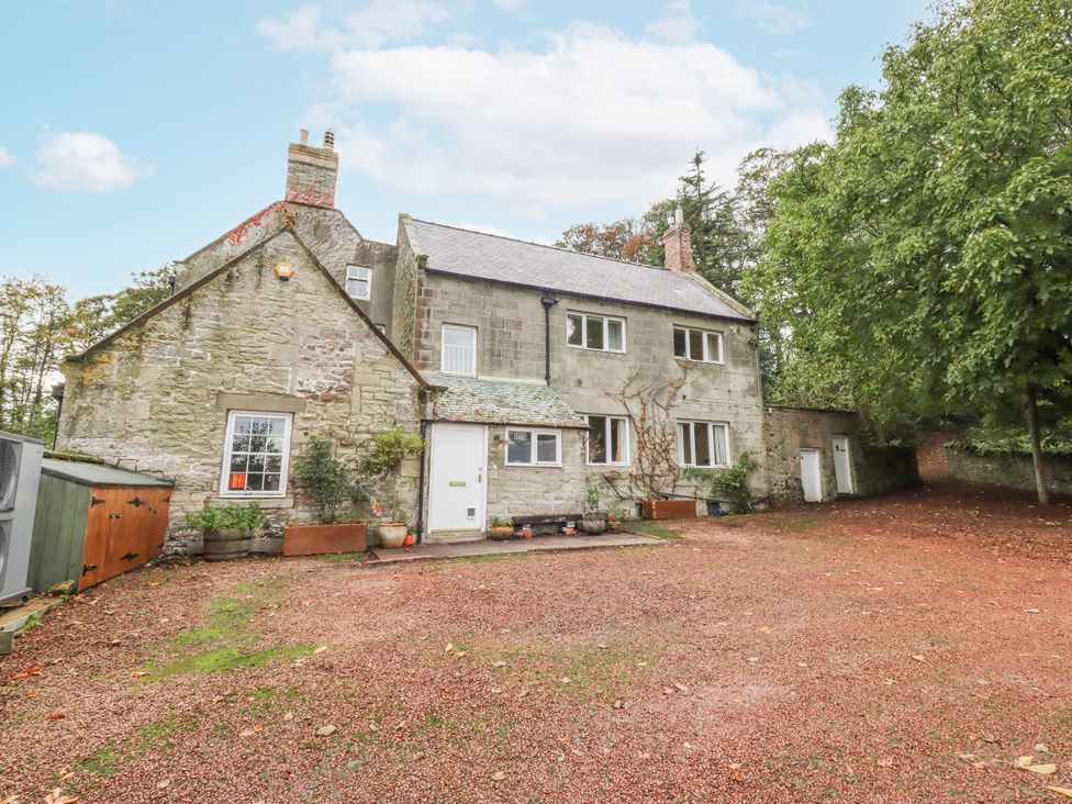 A house with a gravel parking area and trees at Elford Farmhouse Seahouses