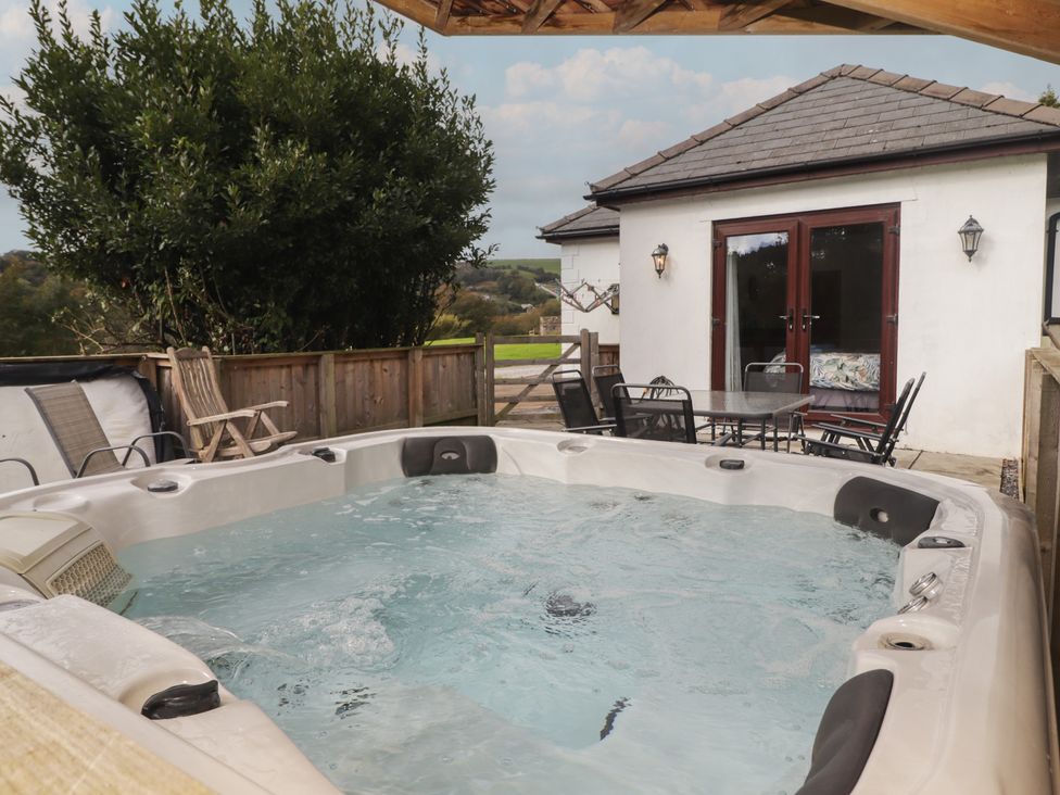 An outdoor area with a hot tub and table with chairs at The Lodge in Bridgend
