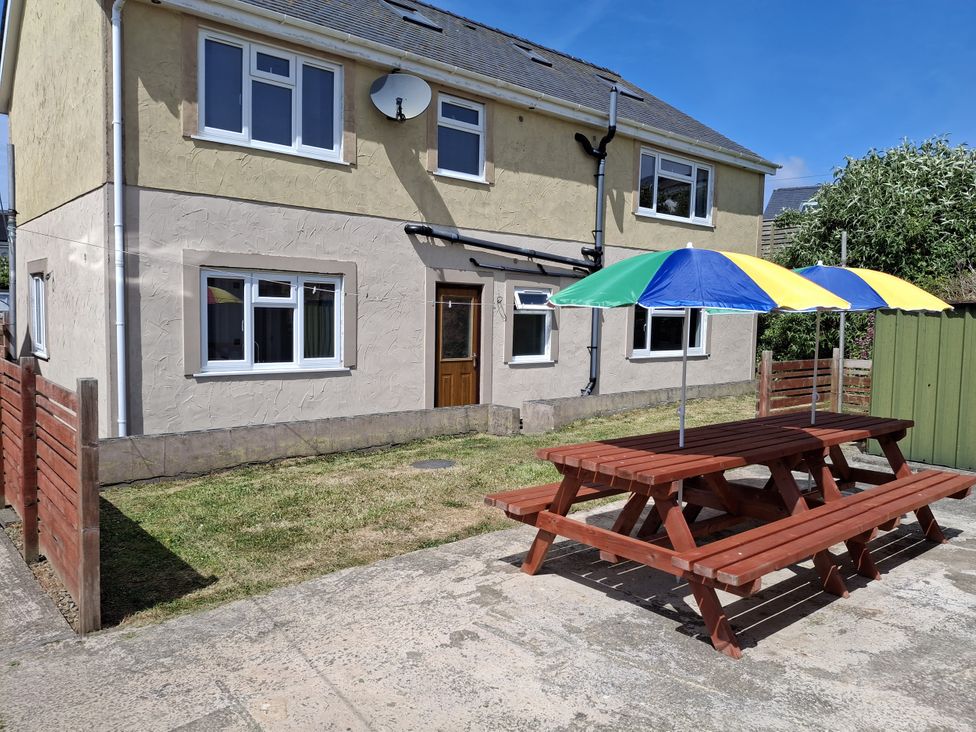 A garden with a patio table and umbrellas at Criw Newydd in Bryncroes near Sarn Meyllteyrn