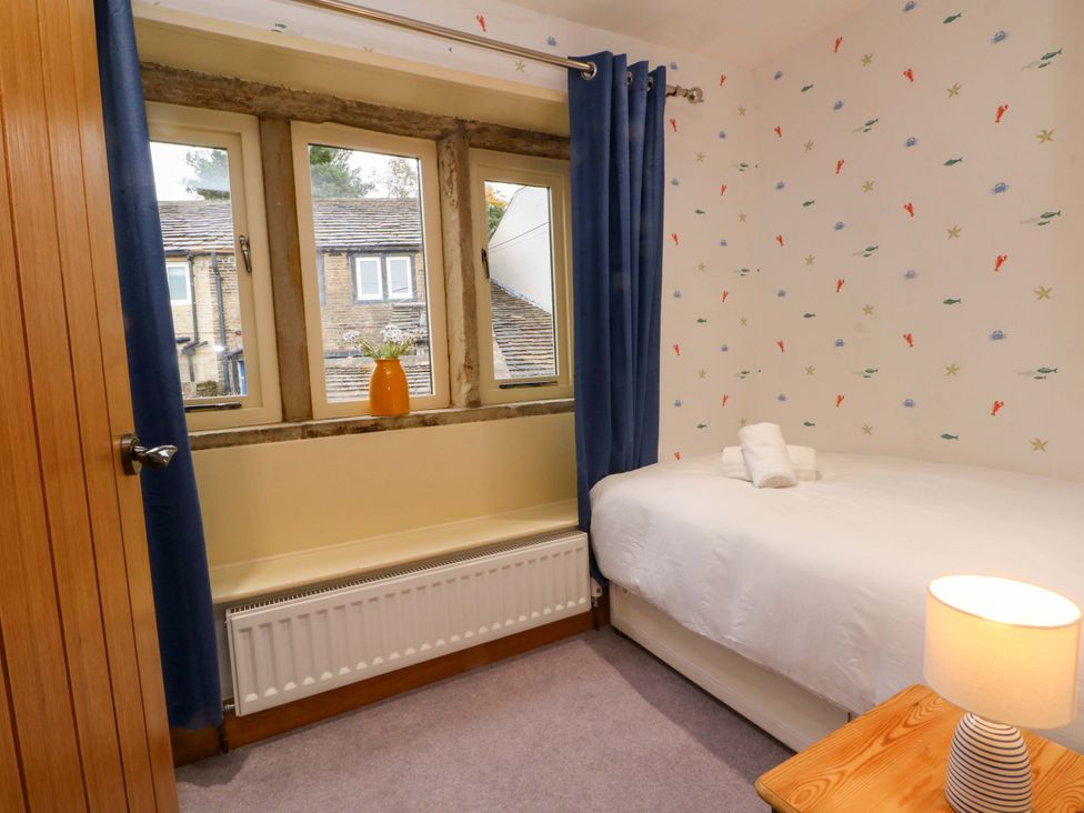 A bedroom with a bed and windows at Stone & Fleece Cottage in Holmbridge