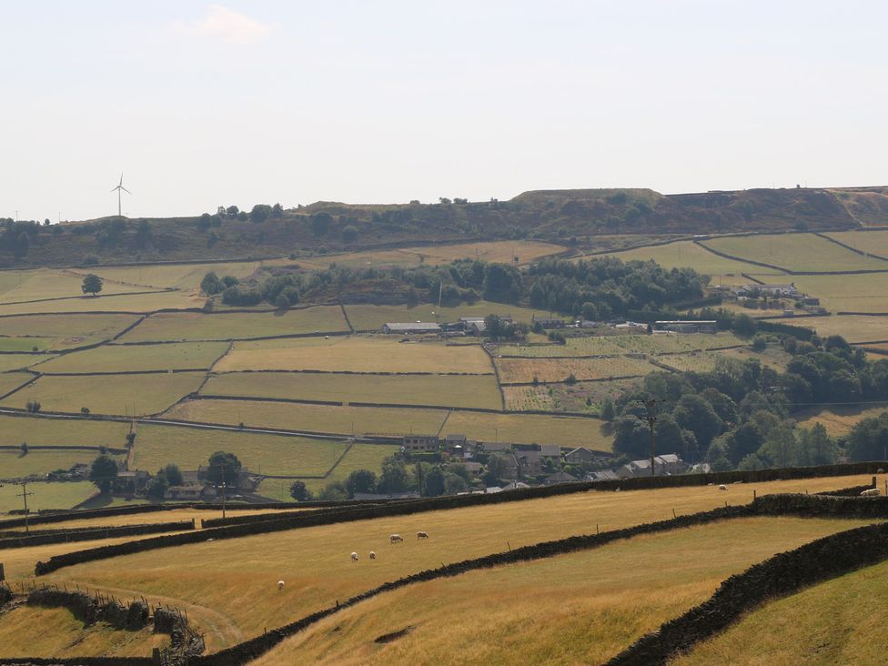 A landscape with fields, trees, houses, and a wind turbine at Stone & Fleece Cottage Holmfirth