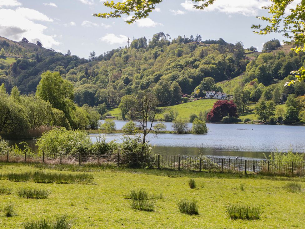 A lake surrounded by trees and grass with a house in the background at The Barn at Grasmere in Grasmere
