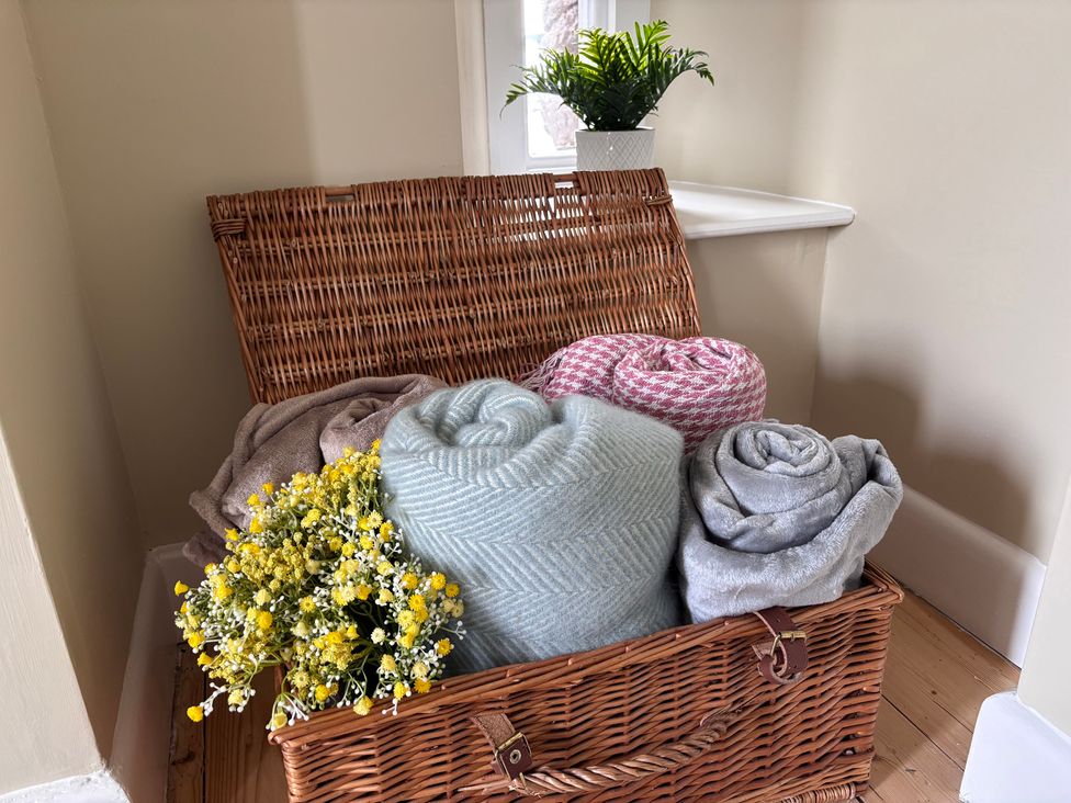 A basket containing rolled blankets and flowers in a living room at The Barn at Grasmere
