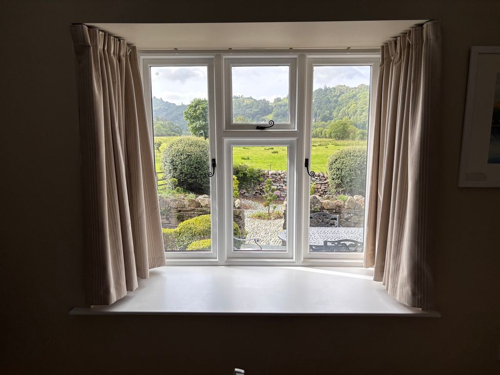 A window with curtains and a view of the garden at The Barn at Grasmere in Grasmere
