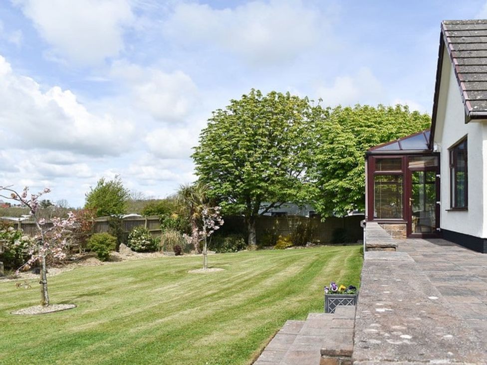A garden with a house and trees at Cae Coch in Brynteg near Benllech