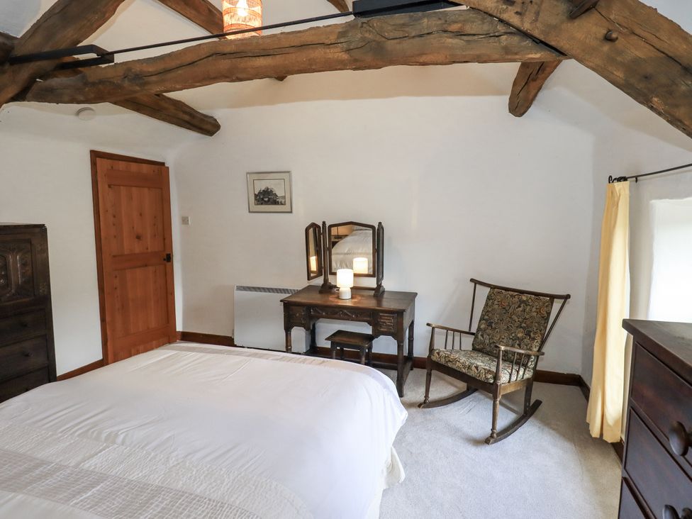 A bedroom with a bed, dressing table, and rocking chair at Chapel Cottage in Ennerdale near Cleator Moor