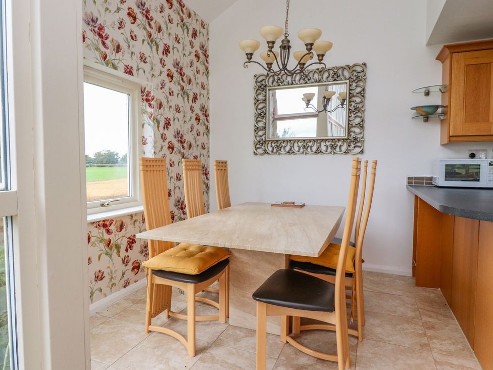 A dining area with a rectangular table and six chairs near a window with floral wallpaper and a mirror at High View Meadows in Kirkby Lonsdale