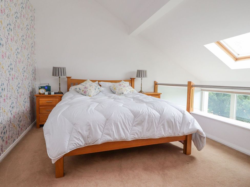 A bedroom with a wooden bed frame white bedding floral pillows beside nightstands with lamps and a window in High View Meadows in Kirkby Lonsdale